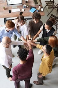 A diverse group of professionals joins hands in a team-building exercise indoors.