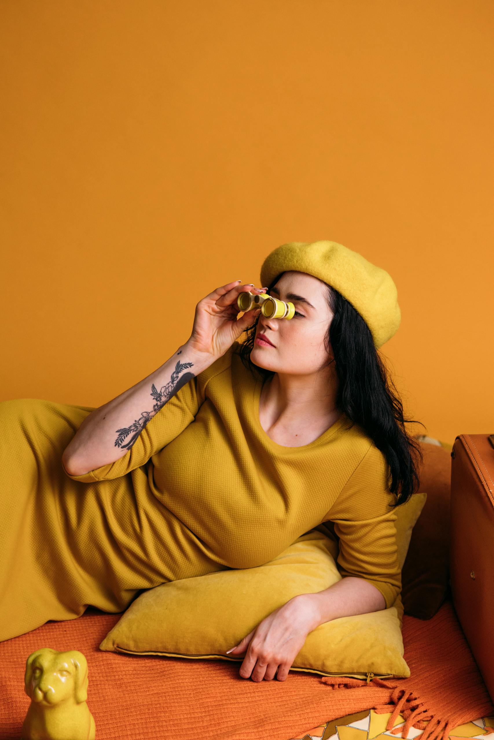 Chic woman posing with binoculars against a vibrant yellow backdrop, symbolizing exploration.